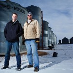Two men standing in front of grain bins.