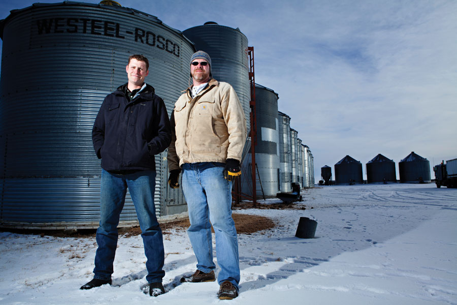 Two men standing in front of grain bins.