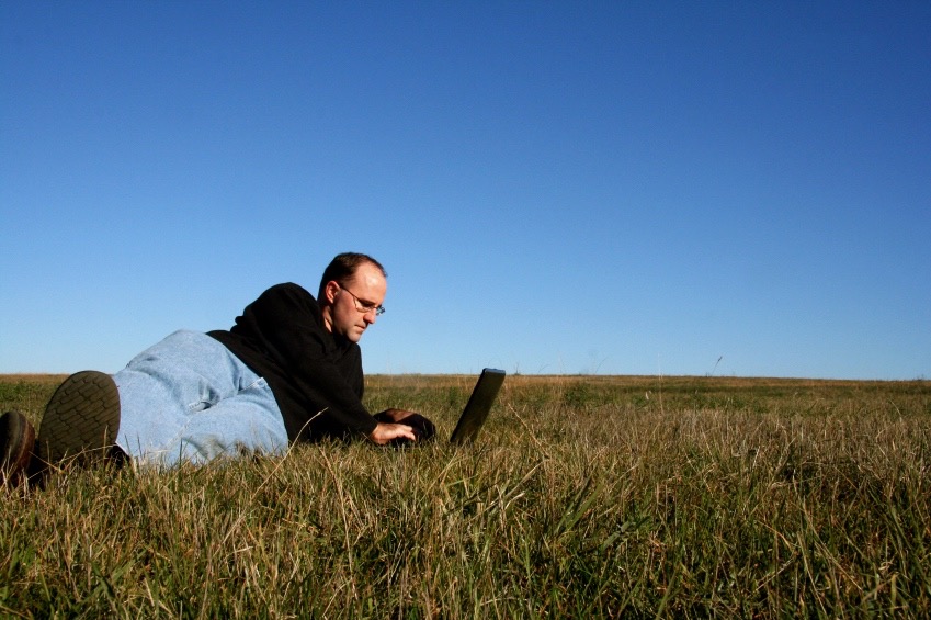 Man at work on laptop lying in grassy field.