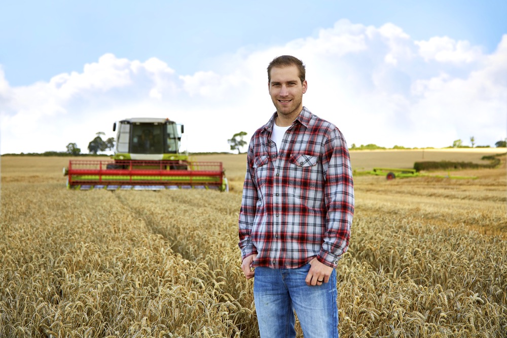 Farmer standing in field with combine harvester behind