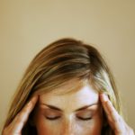 Close-up high section of a young woman touching her head with eyes closed
