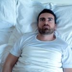 Stressed man trying to sleep in his bed at night