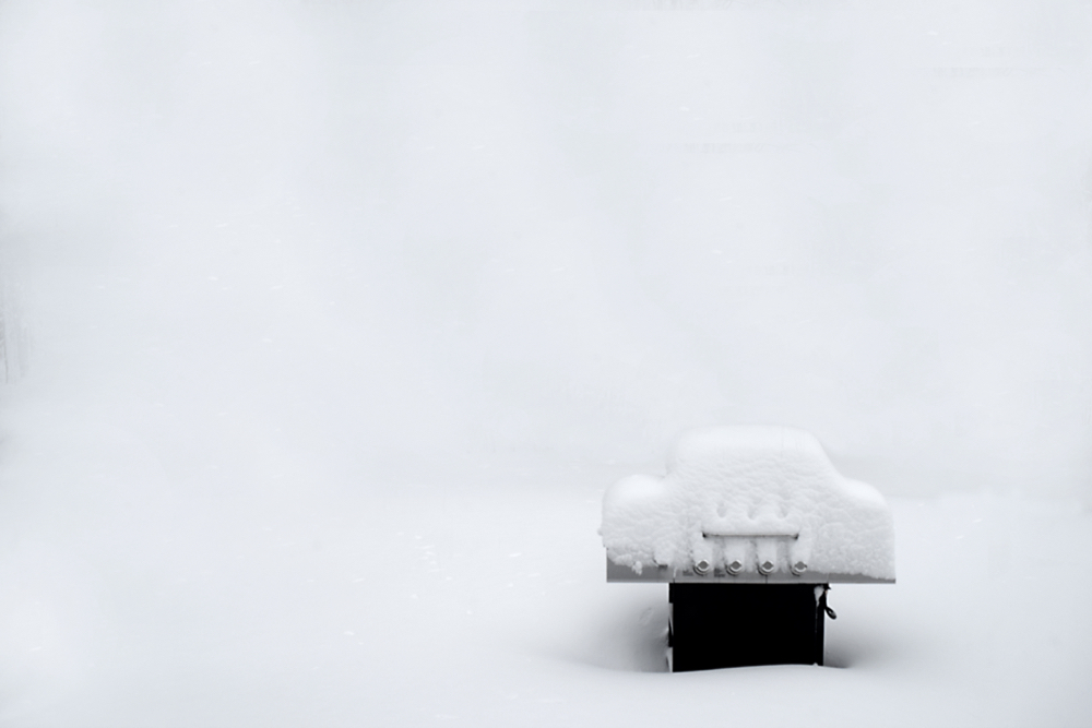 Snow covered outdoor grill during a winter snowstorm frozen cold bar-be-que white-out background type space