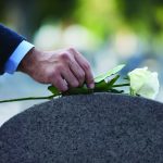 Cropped shot of a man placing a white rose on a grave.