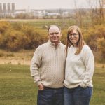 man and woman standing in a farm field with grain silos in the background