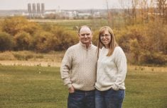 man and woman standing in a farm field with grain silos in the background