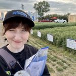 youn woman wearing a ball cap with wheat plots in the background at a farm show