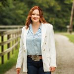 a red-haired woman wearing a white blazer and denim pants