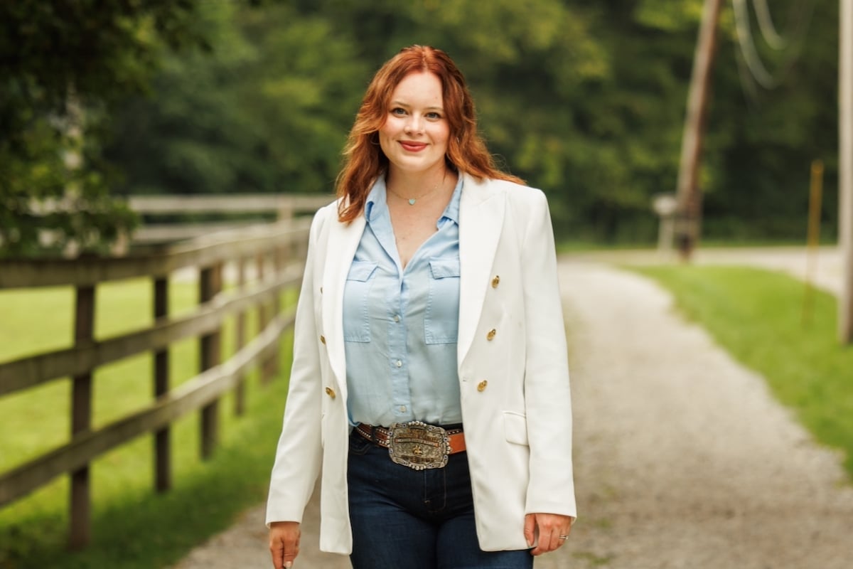 a red-haired woman wearing a white blazer and denim pants
