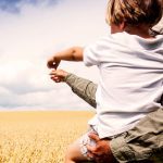 farmer holding a young child in his arms in a field of wheat