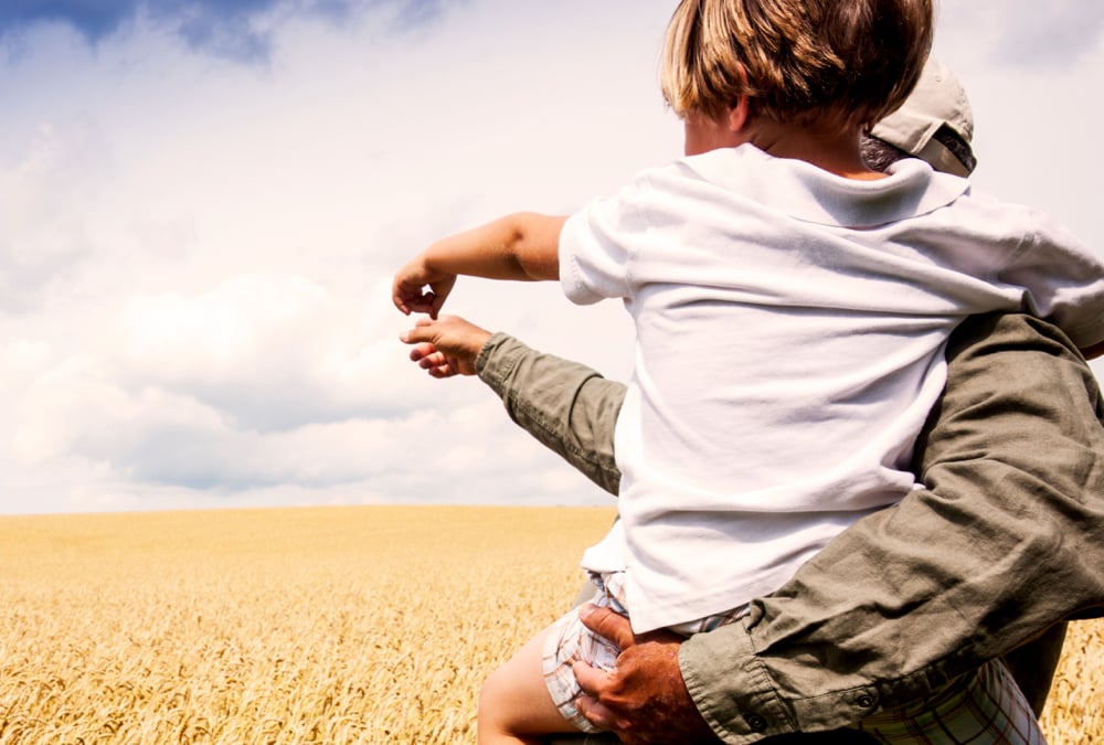 farmer holding a young child in his arms in a field of wheat