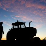 farmer in a field beside a tractor at sunrise