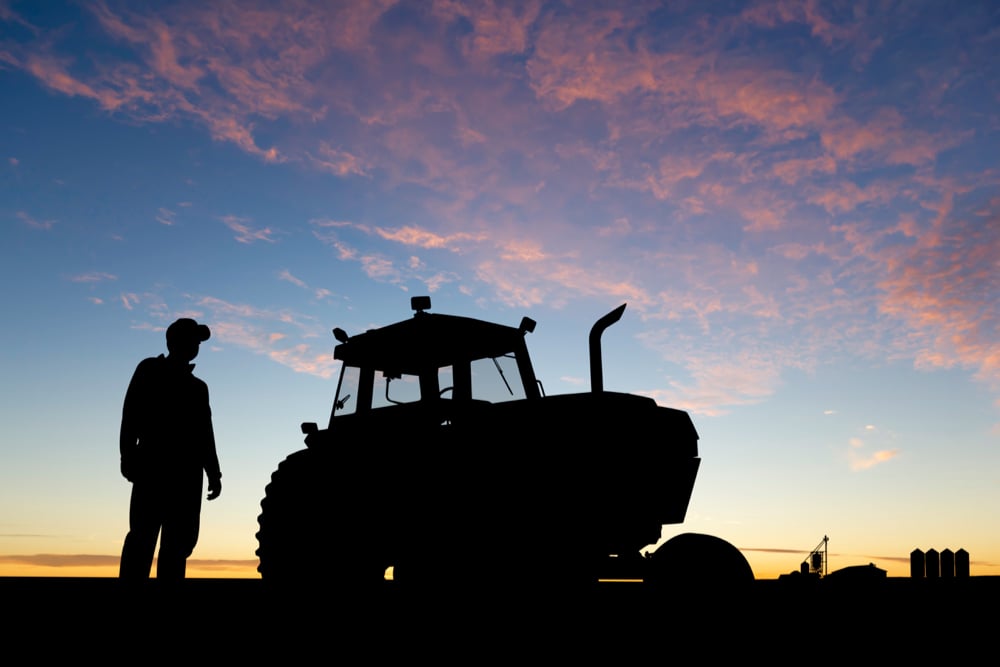 farmer in a field beside a tractor at sunrise