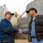 two farmers shaking hands with grain bins in the background