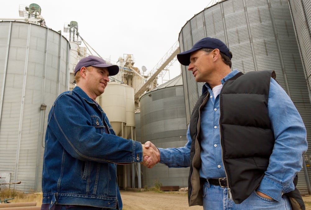 two farmers shaking hands with grain bins in the background