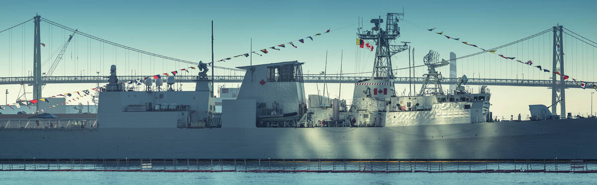 A Canadian Military warship is bathed in sunlight reflected off Purdy's Wharf Towers with the Angus L. MacDonald Bridge in the background.