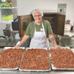 Elisabeth Burrow standing by a table with pans of her roasted nuts