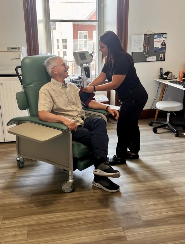 man sitting in a hospital chair with a female physician attending to him