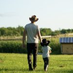 Father and child walking together on a green farm field