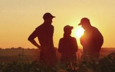 three farmers standing in a field talking silhouetted against a sunset in the background