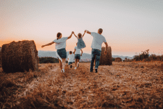 Mom and dad swing daughter in air while walking in a farm field.