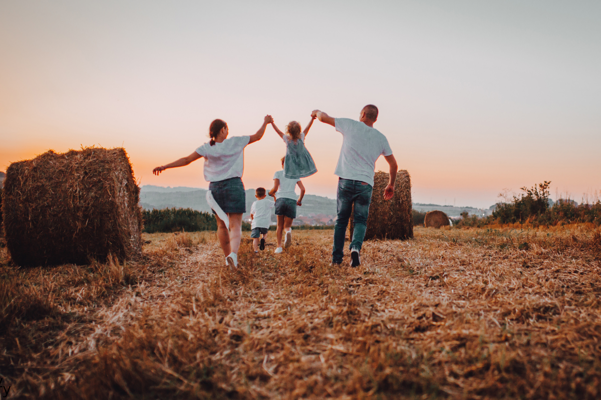 Mom and dad swing daughter in air while walking in a farm field.