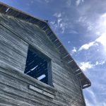 weathered wooden barn with ray of sunshine and blue sky above