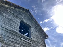 weathered wooden barn with ray of sunshine and blue sky above