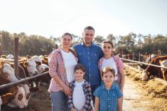 A young happy family of farmers in a cowshed. A smiling woman, a man and three kids in casual clothes take care of the pets on the farm. Mom and dad with their children in the barn