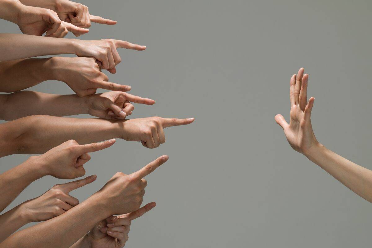 A bunch of hands pointing their fingers at another hand being held up flat.
